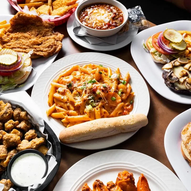 Restaurant table laden with plates of chili, pasta, burgers, and fried food.
