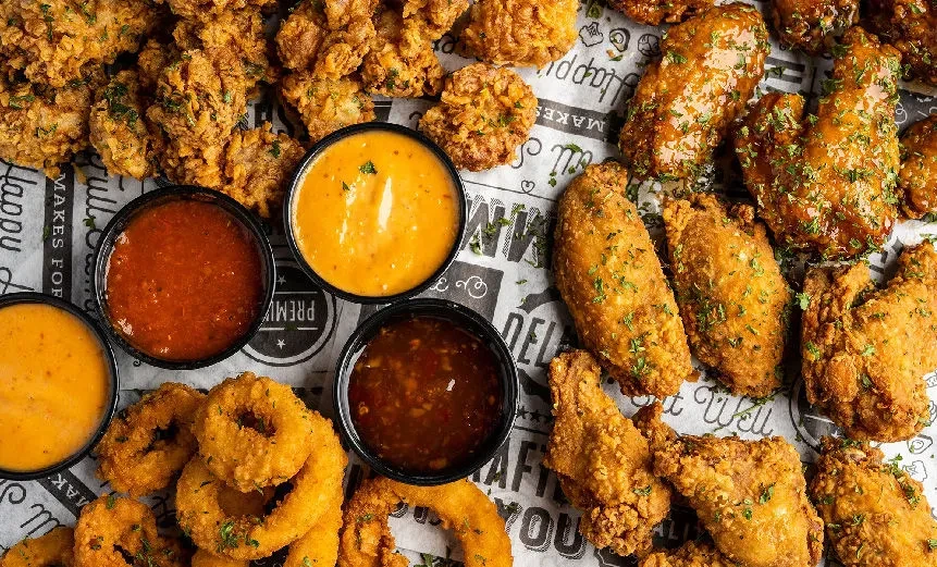 A platter of assorted fried chicken, onion rings, and dipping sauces.