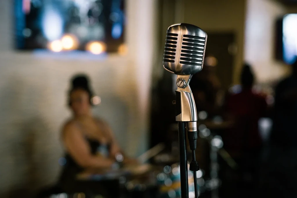 Sharp silver microphone, blurred musician with headphones on a dimly lit stage.