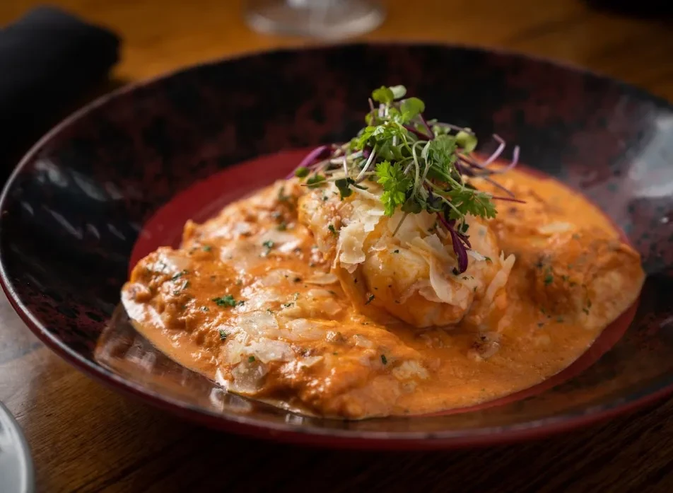 Creamy orange-red dish with Parmesan and greens in a dark bowl.