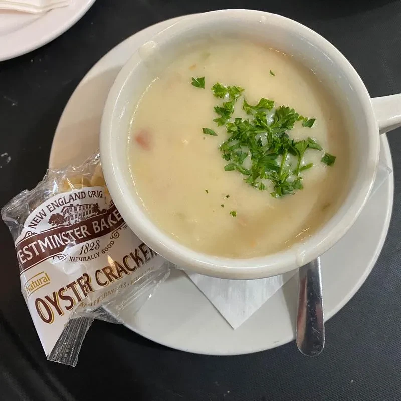Bowl of creamy soup with parsley, oyster crackers, and a spoon.