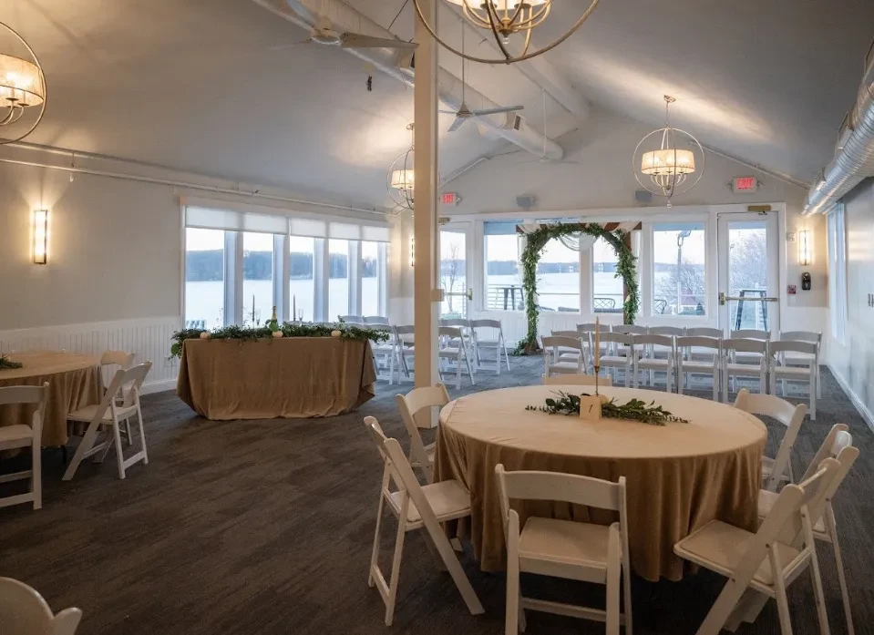 Spacious event hall with round tables, ceremony arch, and scenic water view.