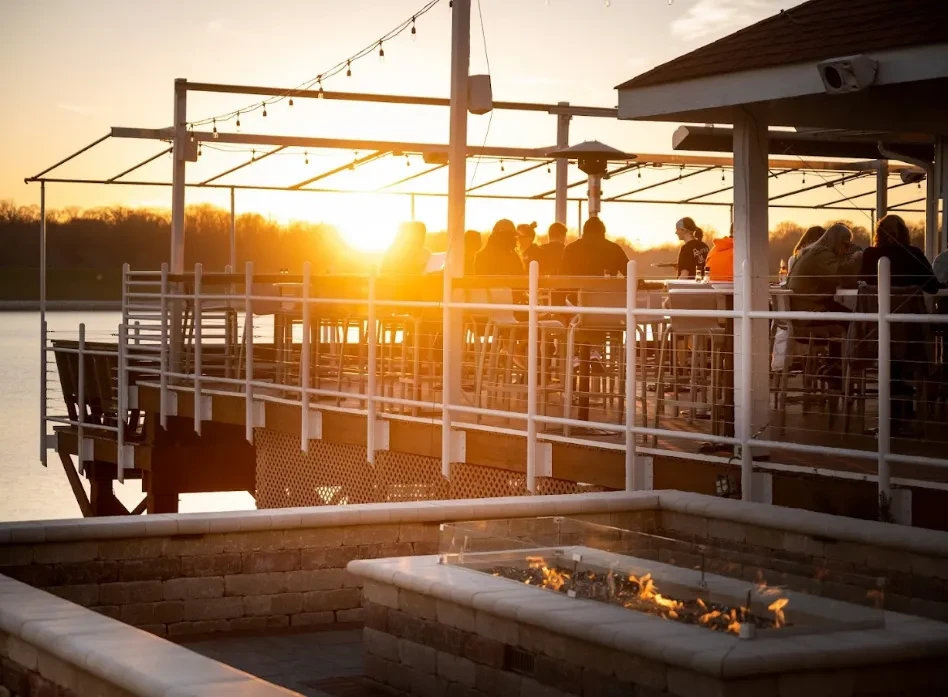 Outdoor fire pit and silhouetted diners on a pier at sunset.