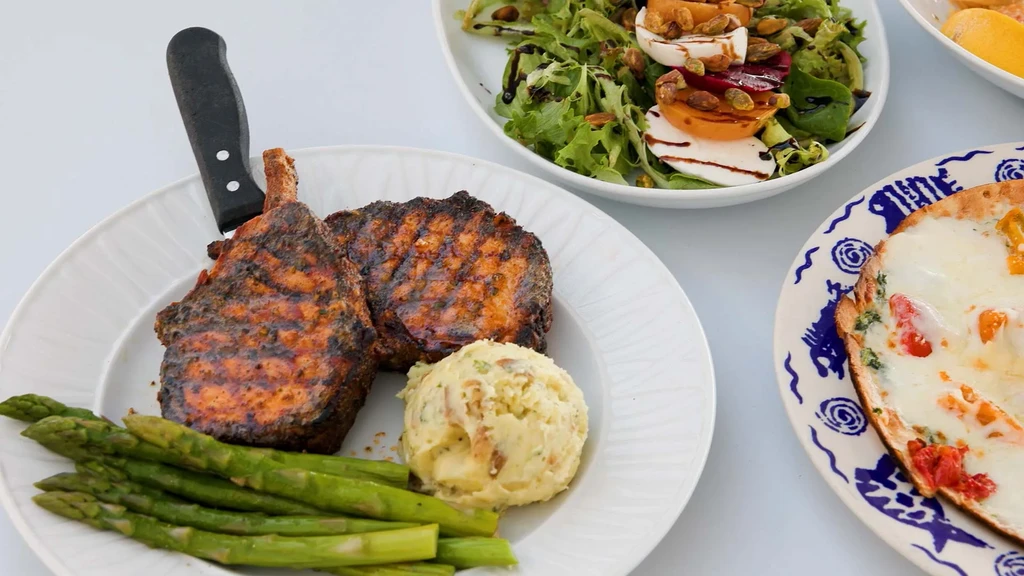 Overhead view of grilled pork chops, mashed potatoes, salad, and flatbread.
