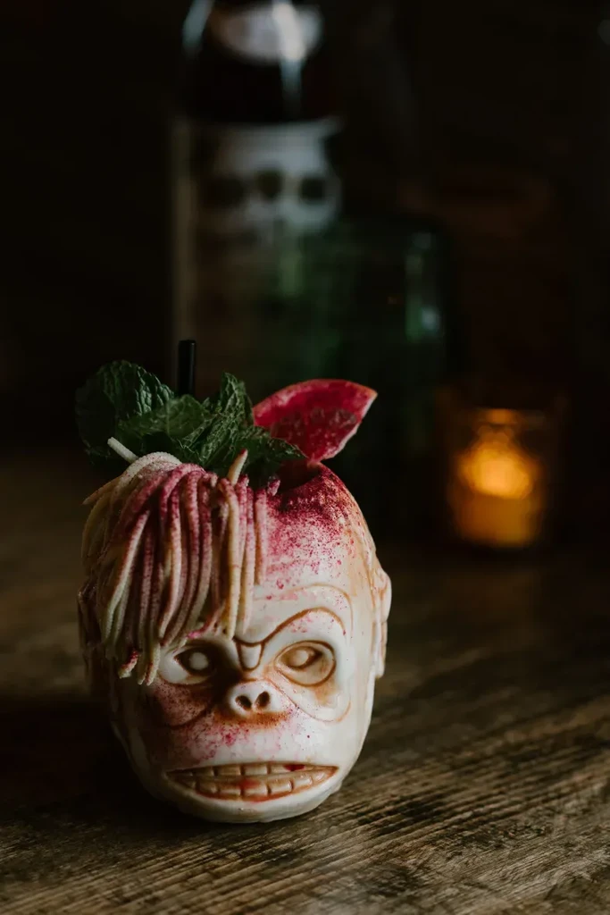 Stylized cocktail in a grimacing monkey head mug with elaborate garnishes.