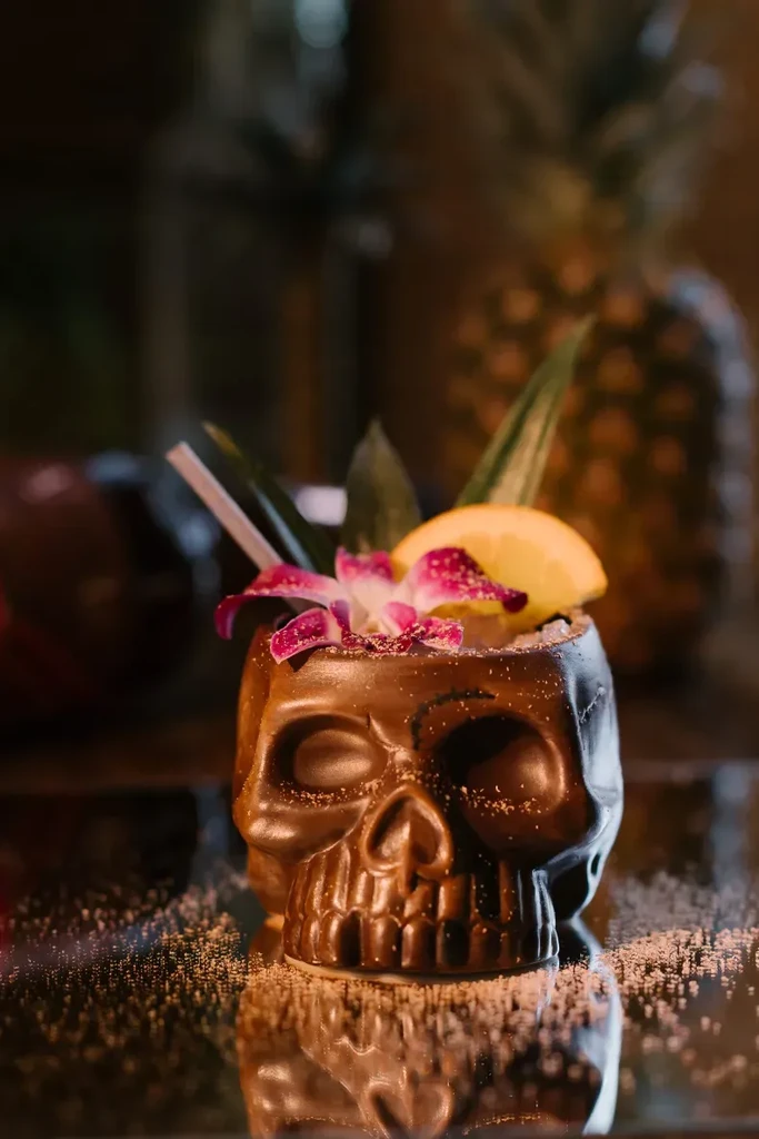 Dark brown skull mug cocktail, tropical garnishes, sugar-dusted and reflective.