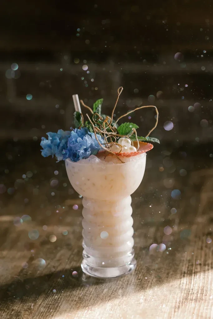 Ribbed glass cocktail with creamy drink, blue petals, and pearls.