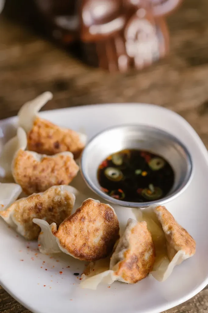 Pan-fried dumplings with crispy golden-brown bottoms and a dark dipping sauce.