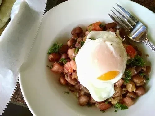 Poached egg on beans, tomatoes, and herbs with a fork.