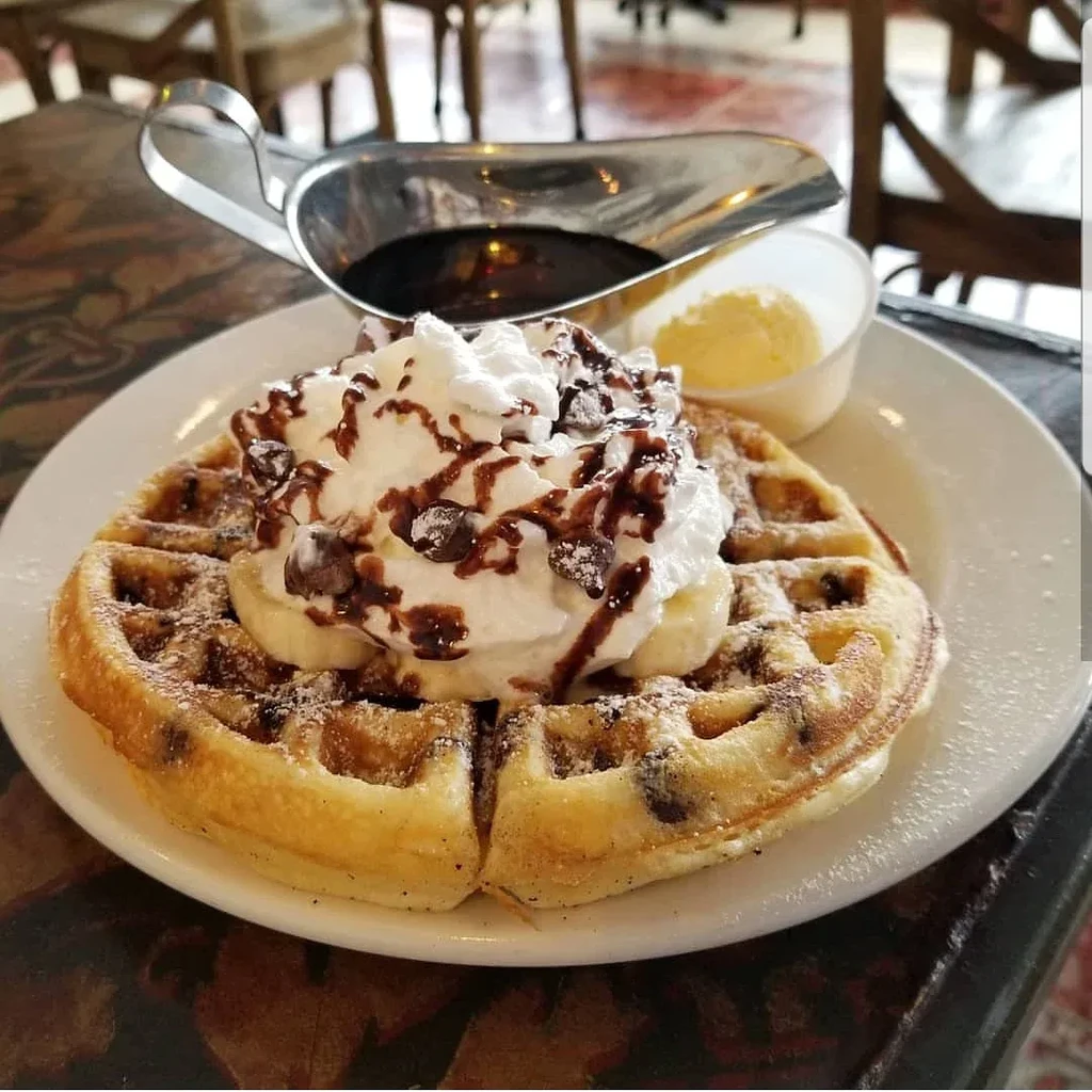 Golden-brown waffle with whipped cream, bananas, chocolate chips, and sauce.
