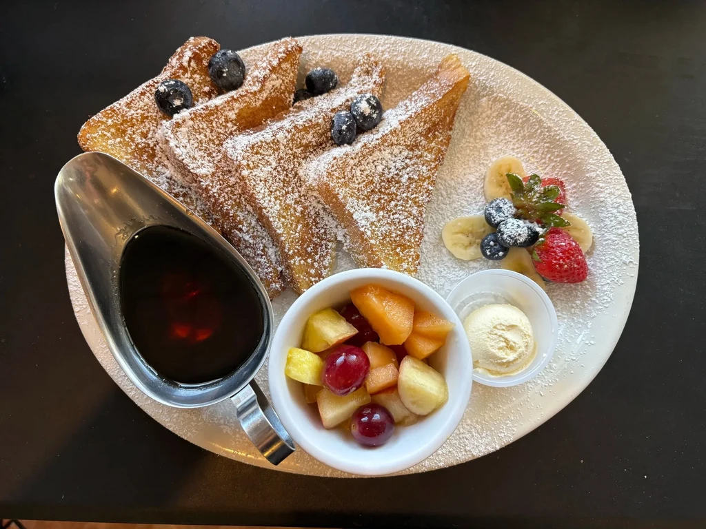 Powdered French toast with fruit salad, berries, syrup, and cream.