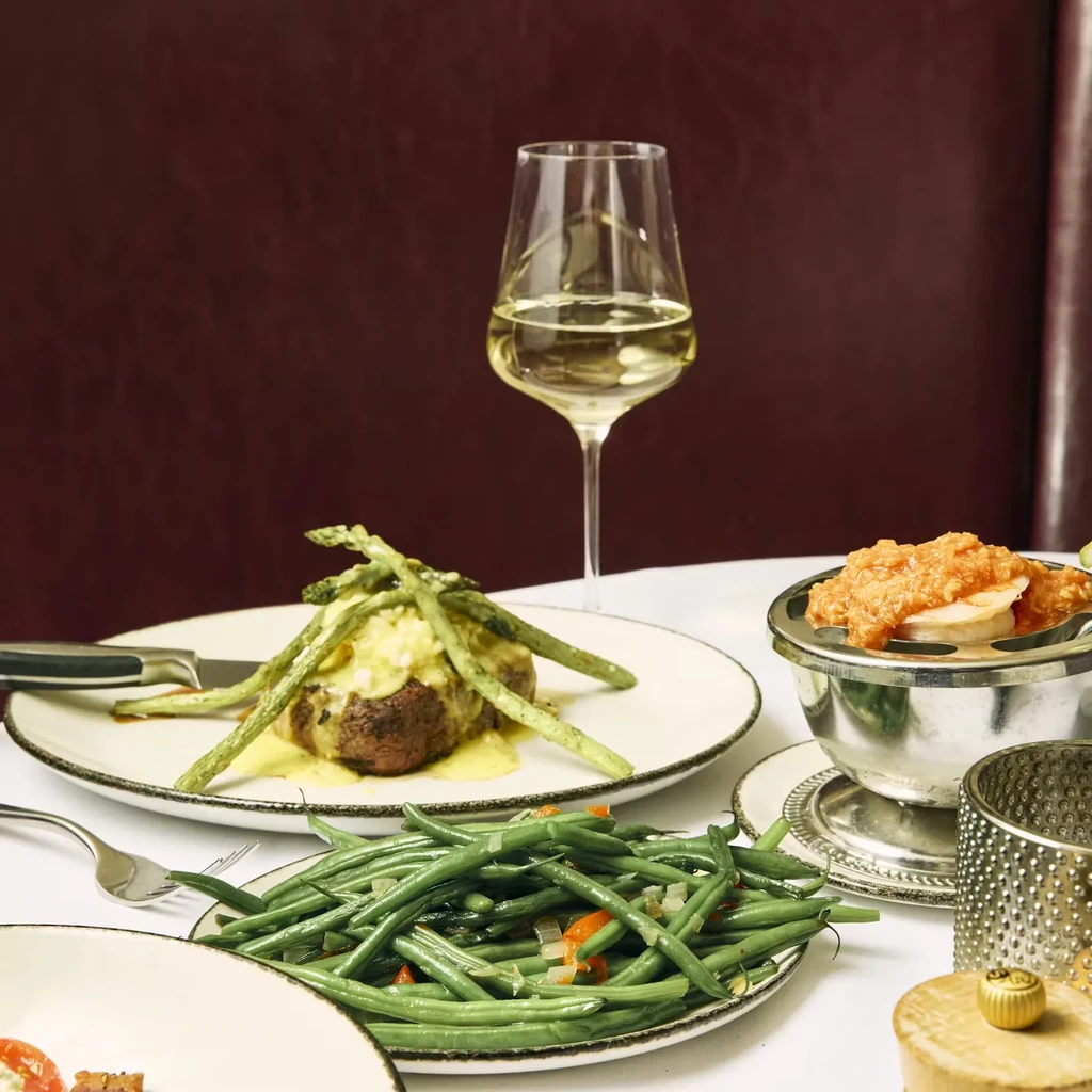Steak with asparagus, green beans, white wine on an upscale dining table.