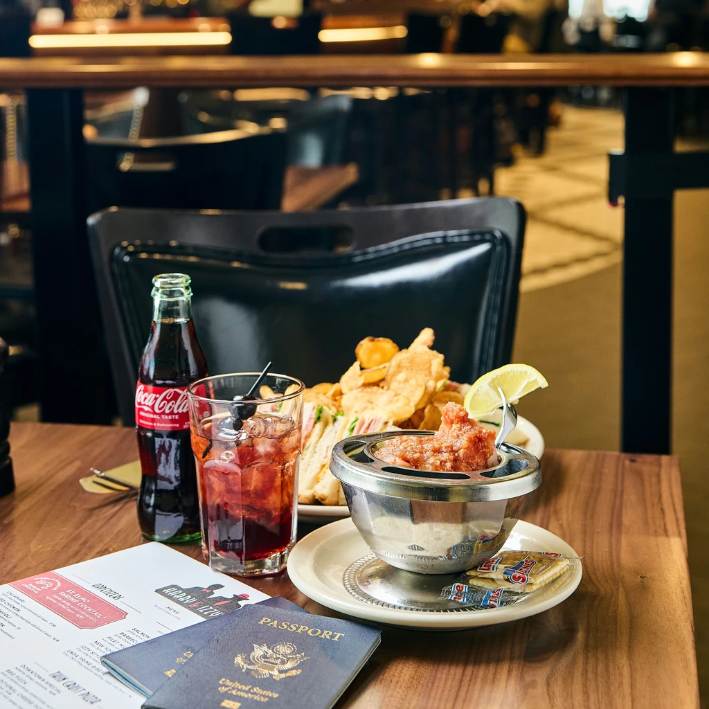 Restaurant table: Coca-Cola, amber drink, seafood, sandwich, menu, passports.