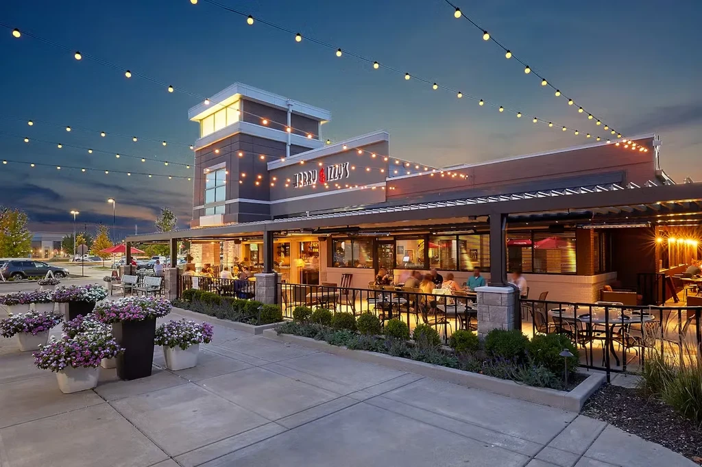 JERRY & IZZY'S restaurant exterior: bustling patio under string lights at dusk.