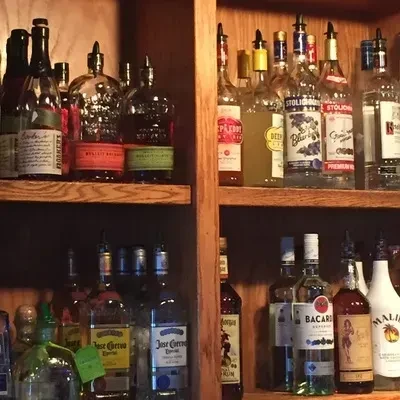 Dimly lit wooden bar shelf displaying diverse liquor bottles with pourers.