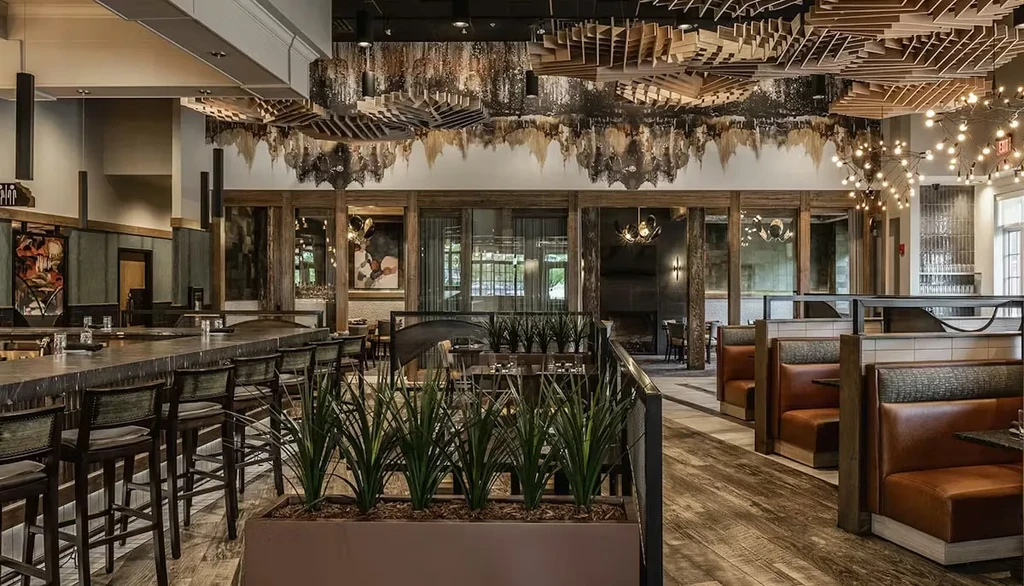 Modern restaurant interior: dark bar, green stools, leather booths, ornate wooden ceiling.