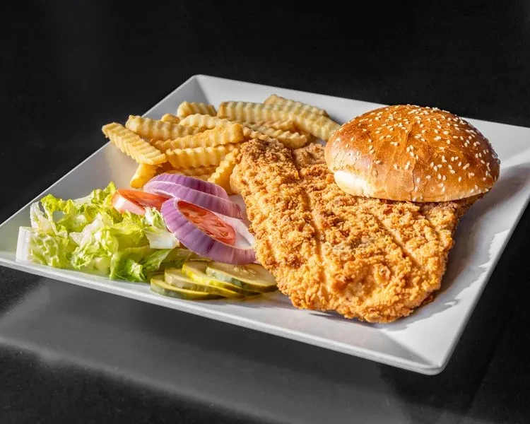 Crispy fried cutlet, bun, crinkle fries, and fresh salad on white plate.