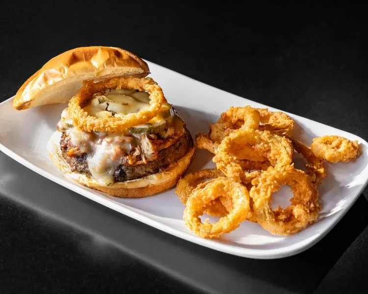 Gourmet burger with melted cheese and side of onion rings.