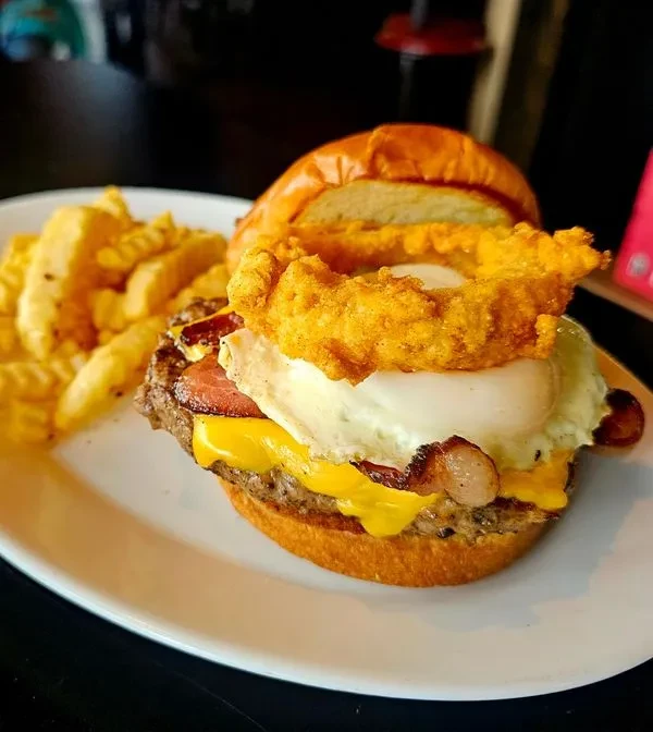 Burger with fried egg, bacon, cheese, onion ring, and crinkle fries.