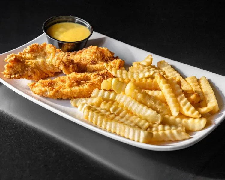 Plate of three crispy chicken tenders, crinkle-cut fries, and dipping sauce.