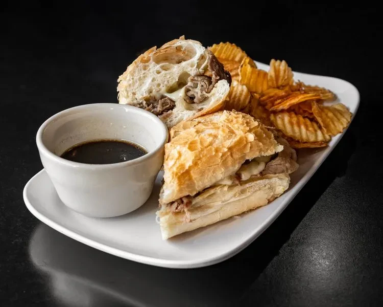 French dip sandwich, ridged chips, and au jus on a white plate.