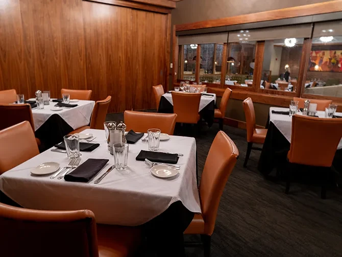 Upscale restaurant dining room with set tables, wood paneling, and warm lighting.