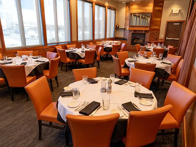 Empty, well-lit dining room with set tables, orange chairs, and fireplace.