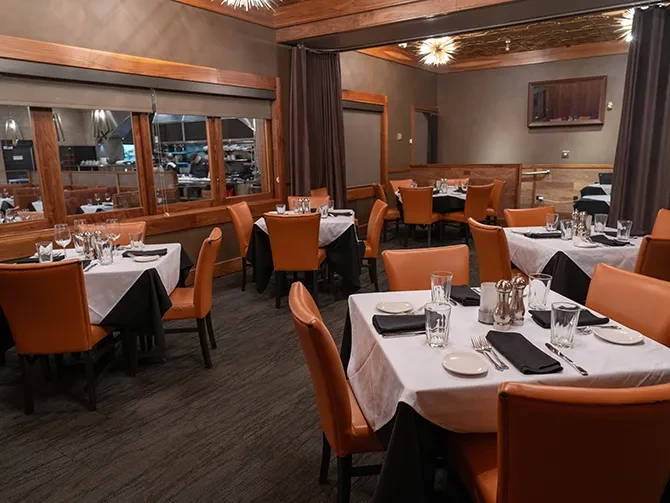 Restaurant dining room with set tables, orange chairs, and kitchen window.