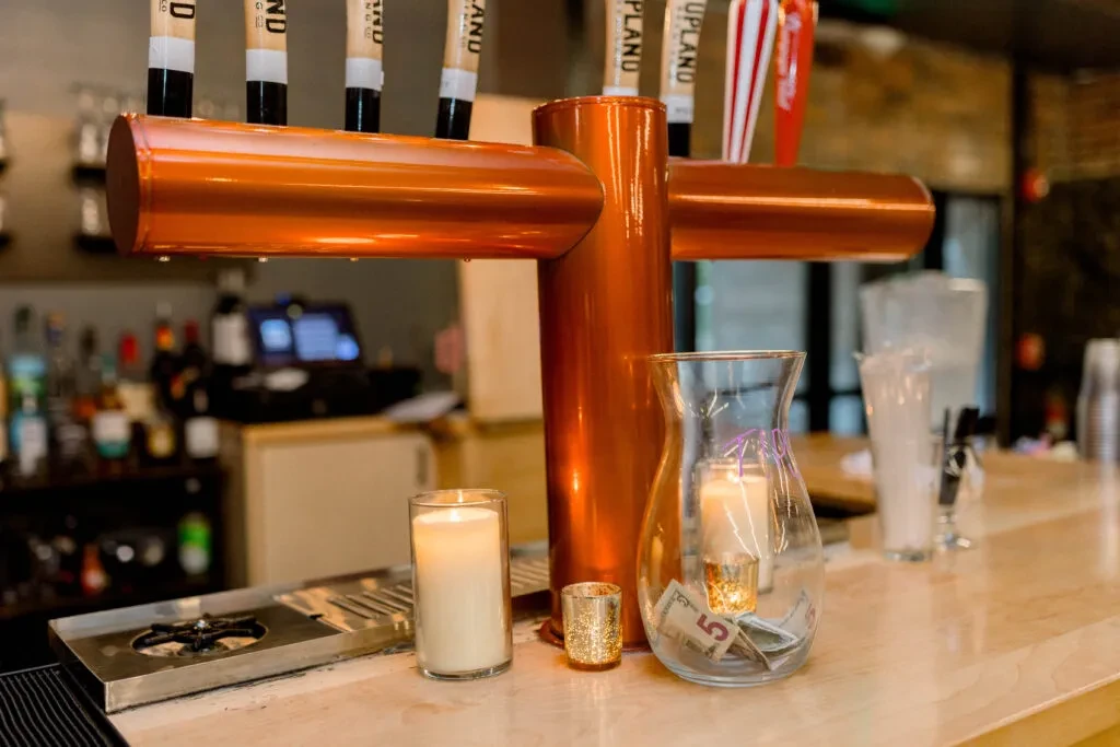 Shiny copper beer taps, candles, and tip jar on bar counter.