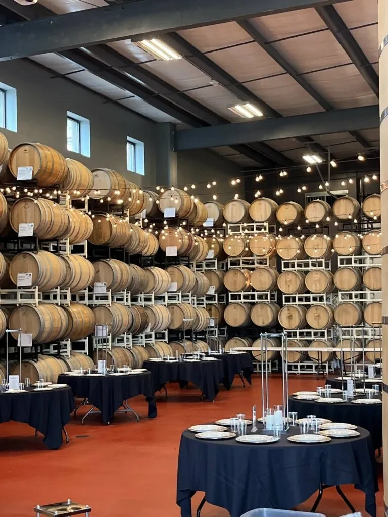 Industrial event space with stacked barrels, set tables, and string lights.