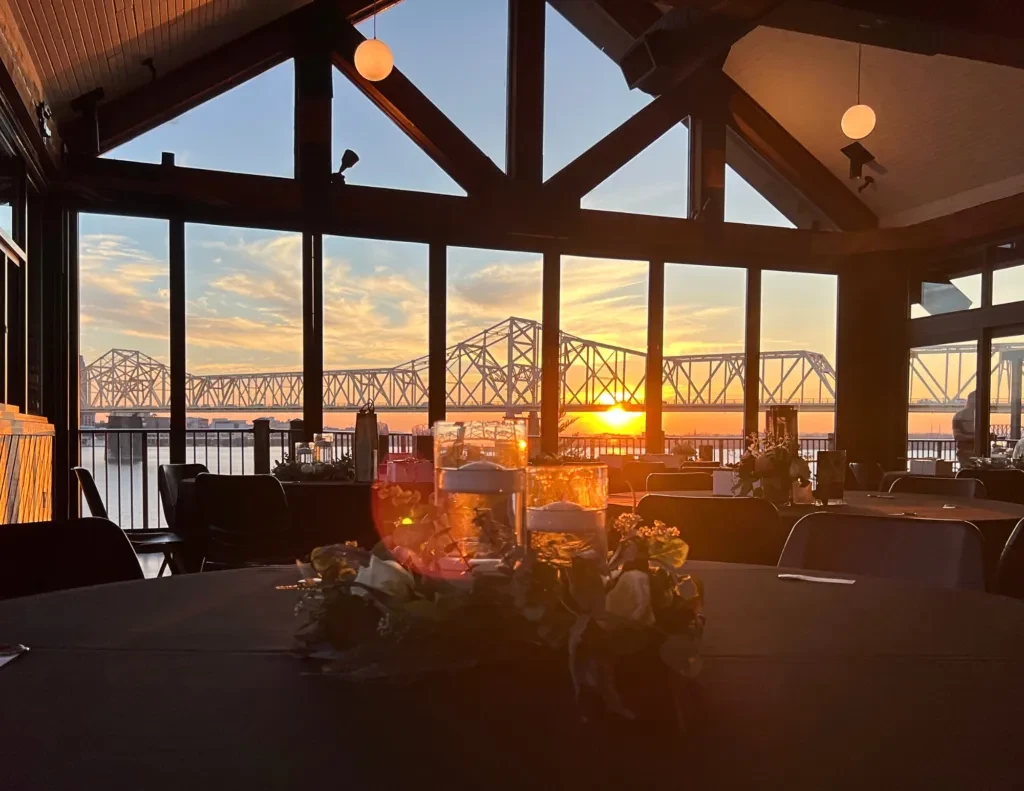 Empty dining room overlooking a metal truss bridge during sunset.
