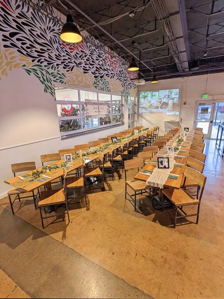 Spacious, decorated event hall with tables, colorful mural, and industrial ceiling.