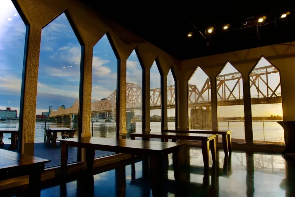 Arched restaurant windows frame a river, steel bridge, and city skyline.