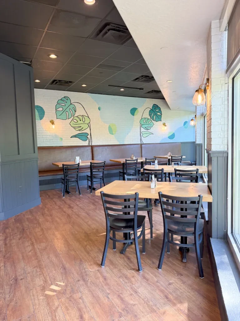 Empty modern restaurant dining area with tables, booths, and leaf mural.