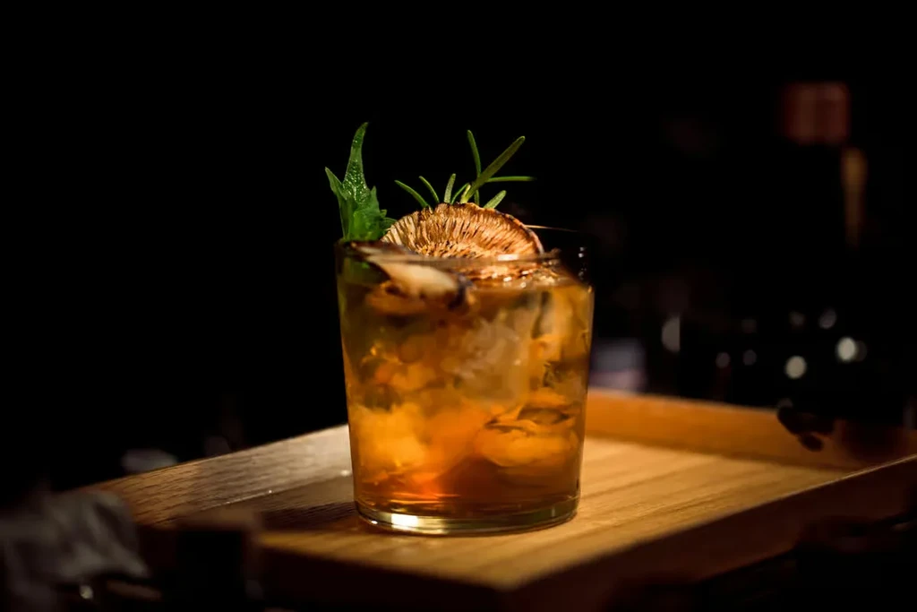 Amber cocktail in glass with ice, dried citrus, and rosemary garnish.