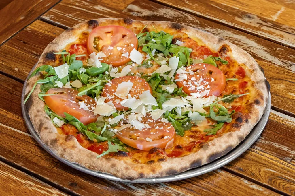 Freshly baked pizza with arugula, tomato, and cheese on a silver pan.