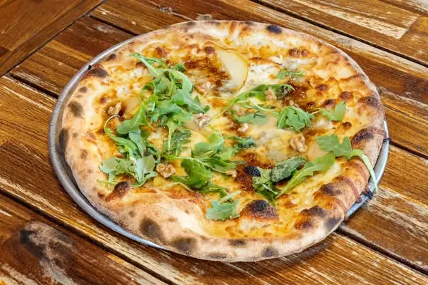 Whole pizza with cheese, pear, walnuts, and arugula on a wooden table.