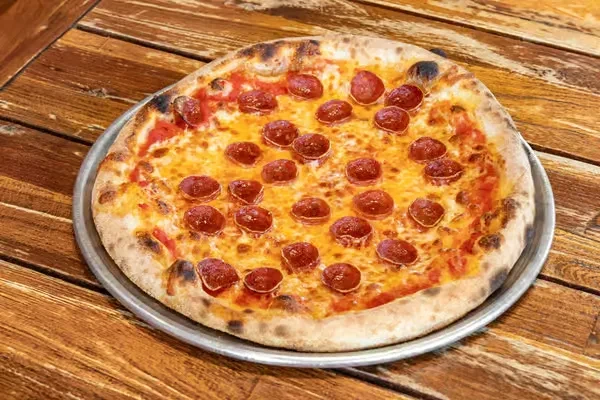 Whole Neapolitan pepperoni pizza on a metal pan and rustic table.