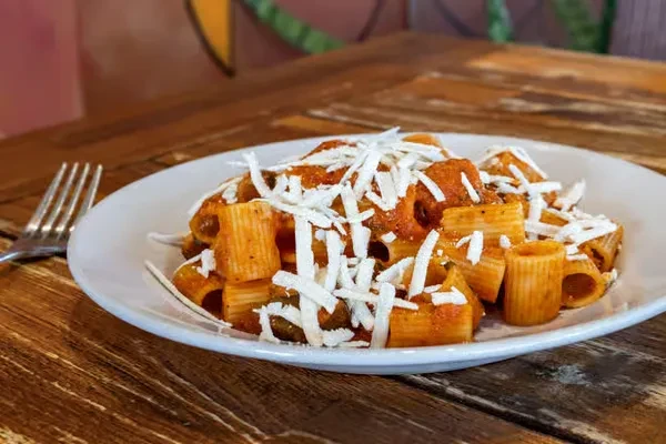 Close-up of rigatoni pasta with red sauce and shredded white cheese.
