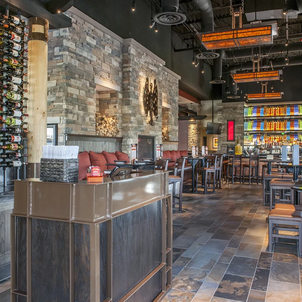 Warm, modern restaurant interior with stone fireplace, wine rack, and backlit bar.