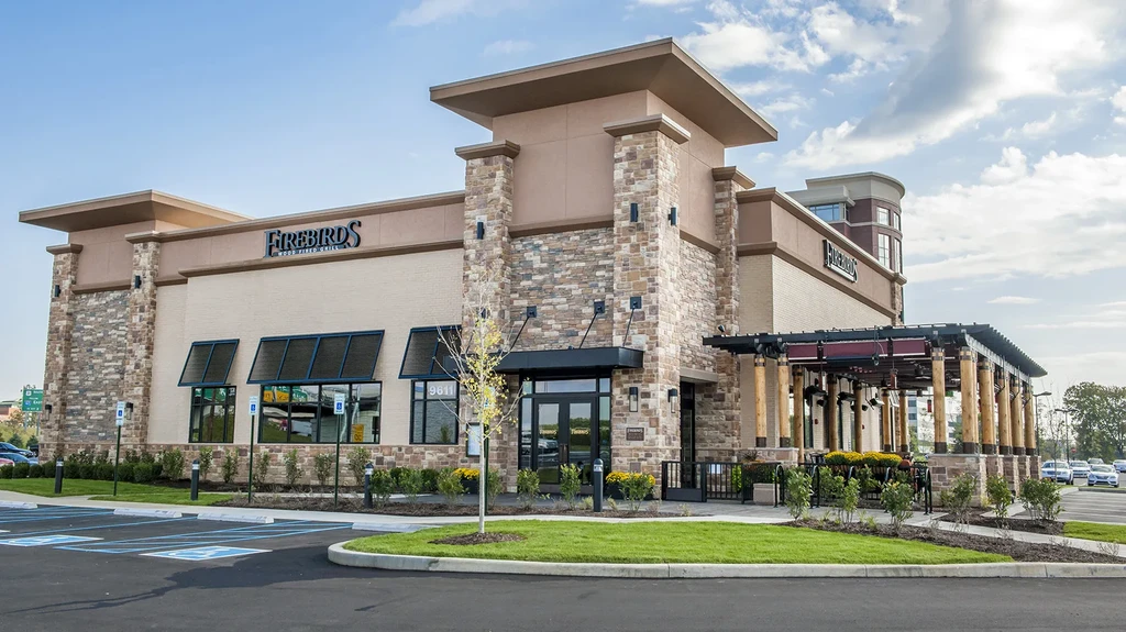 Modern Firebirds Wood Fired Grill building, stone facade, with outdoor patio.