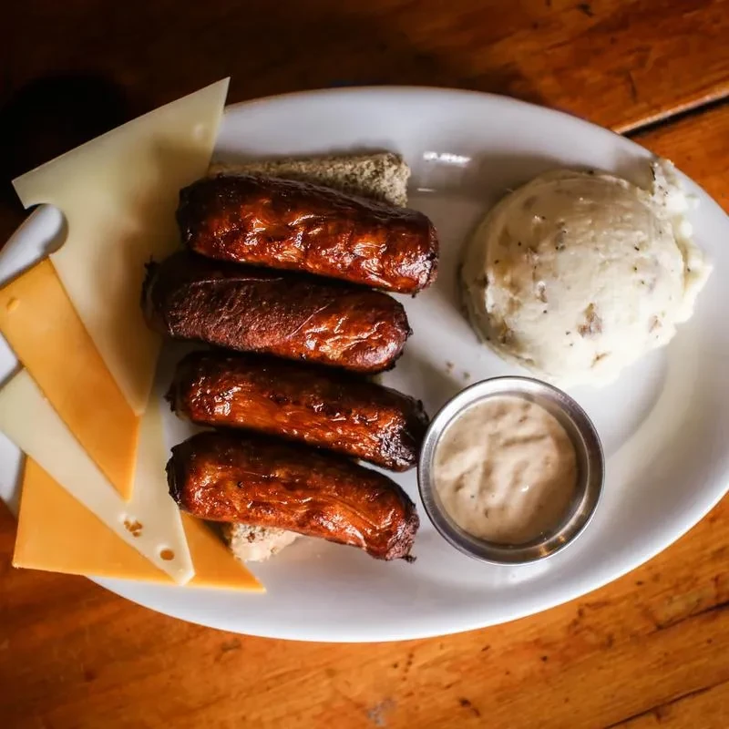 Grilled sausages on toast with cheese, mashed potatoes, and dipping sauce.