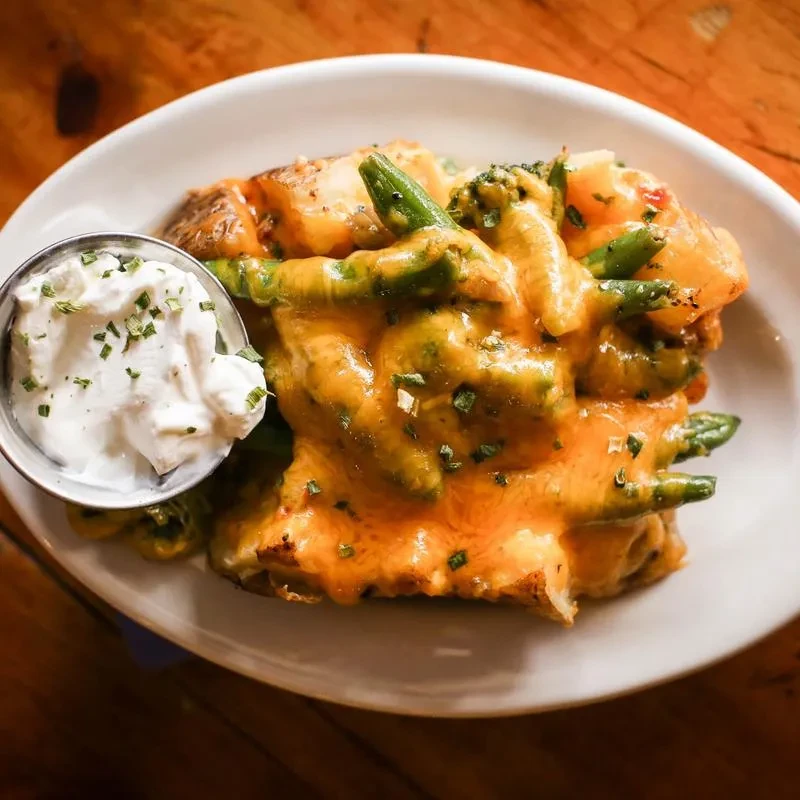 Close-up: Baked potato with melted cheese, green vegetables, and sour cream.
