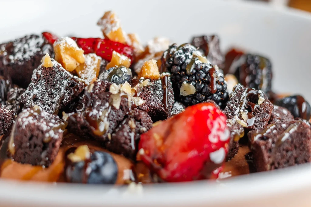 Brownie squares with fresh berries, nuts, powdered sugar, and caramel drizzle.