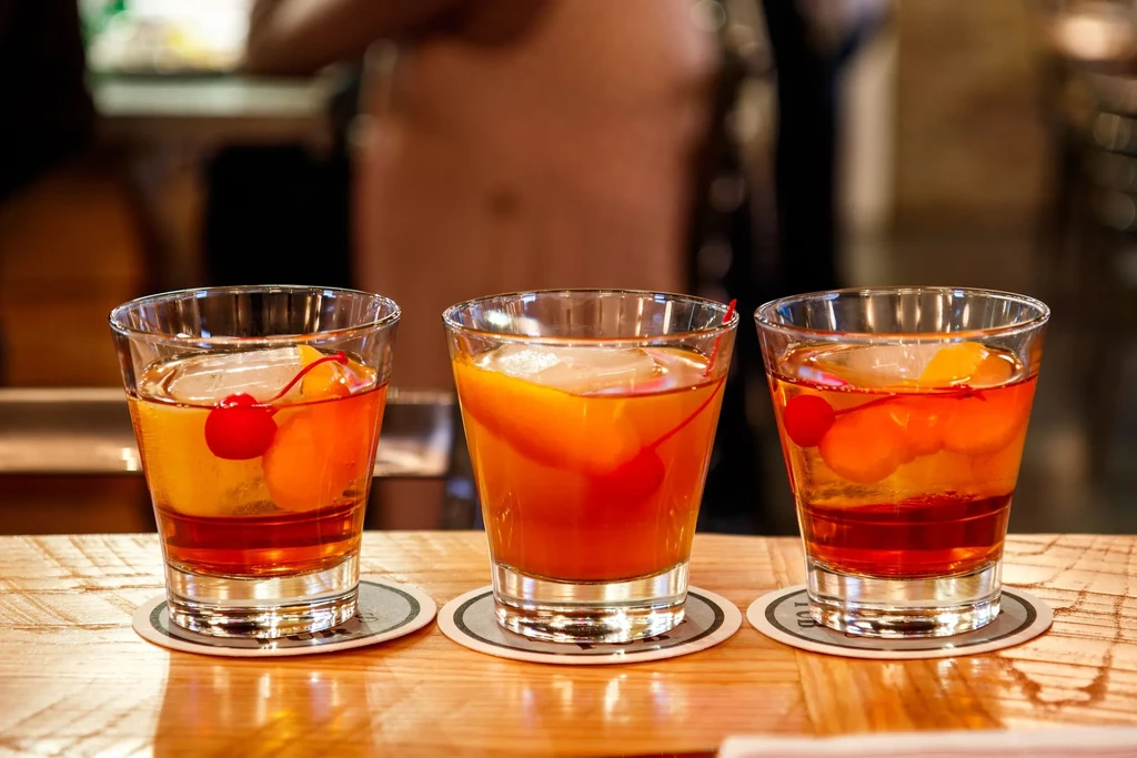 Three Old Fashioned cocktails with cherries, orange, and ice cubes.