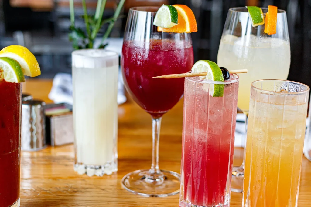 Five vibrant, garnished cocktails on a wooden table.