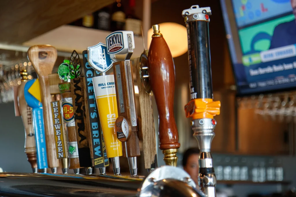 Row of diverse beer tap handles featuring specific breweries and a car.