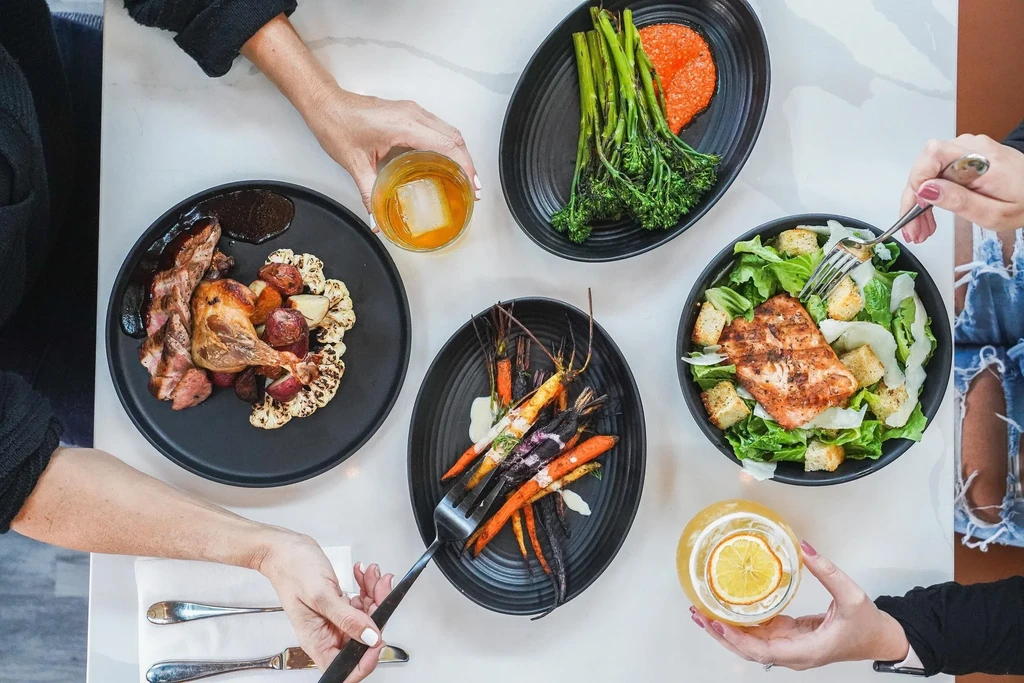 Overhead shot of colorful dishes, drinks, and hands on a restaurant table.