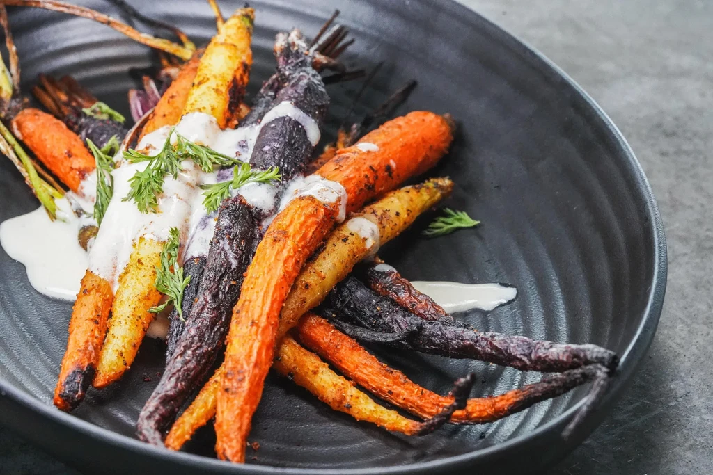 Roasted heirloom carrots with creamy sauce and fresh herbs on a dark plate.