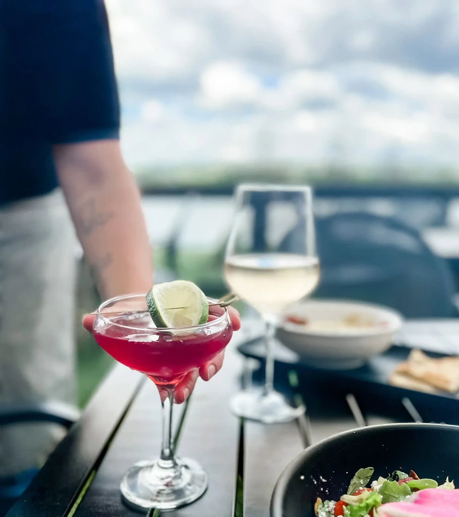 Vibrant red cocktail with lime, held by a hand at outdoor dining.